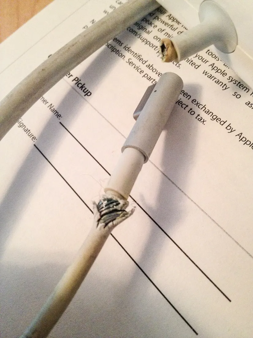A MagSafe cable torn open right behind the connector, lying on an Apple repair form